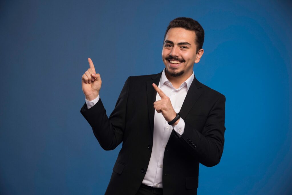 Smiling businessman in suit pointing upwards on blue background